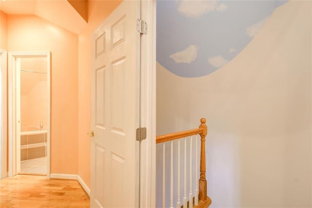 hallway featuring an upstairs landing, baseboards, and light wood finished floors