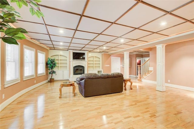 living room with built in features, wood finished floors, coffered ceiling, ornate columns, and a fireplace with raised hearth