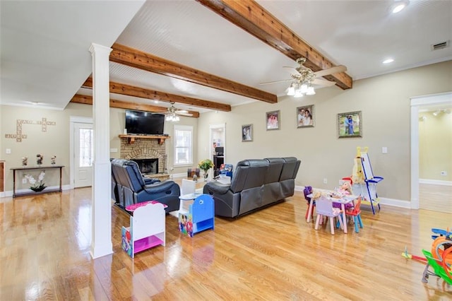 living room featuring a stone fireplace, wood finished floors, visible vents, and a ceiling fan