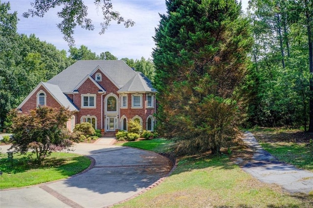 view of front facade with brick siding, driveway, and a front lawn