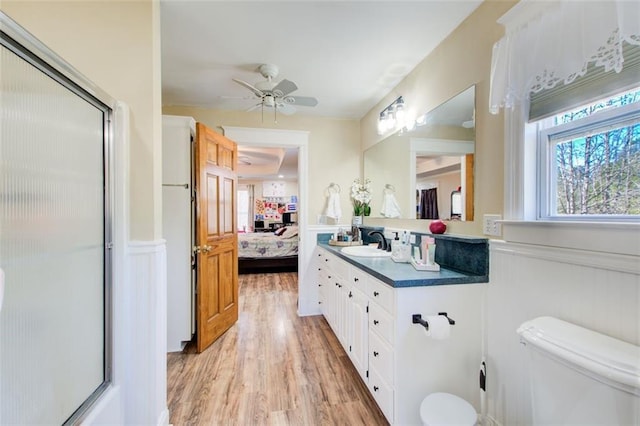 ensuite bathroom with vanity, wood finished floors, a shower with shower door, a wainscoted wall, and connected bathroom