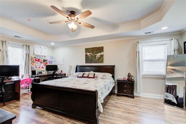 bedroom with a tray ceiling, multiple windows, and light wood finished floors