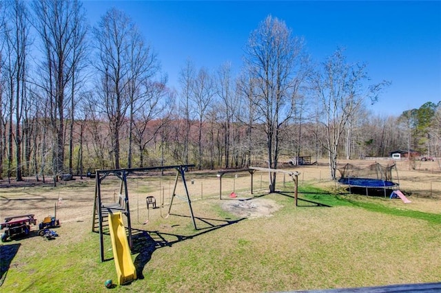 view of yard with a forest view, a playground, and a trampoline