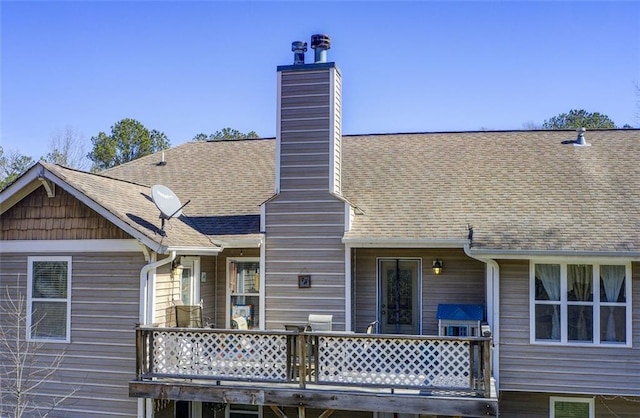 back of house with a chimney and a shingled roof