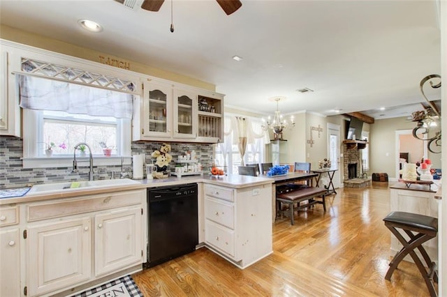 kitchen with light wood finished floors, a peninsula, a sink, decorative backsplash, and black dishwasher