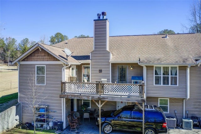 back of house with roof with shingles, central AC, and a chimney