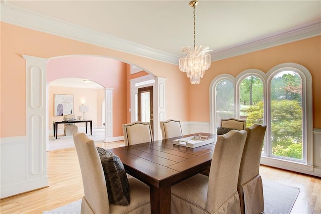 dining space featuring light wood-style flooring, a healthy amount of sunlight, arched walkways, and ornate columns