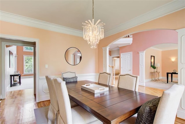 dining area featuring light wood-type flooring, ornamental molding, an inviting chandelier, arched walkways, and ornate columns