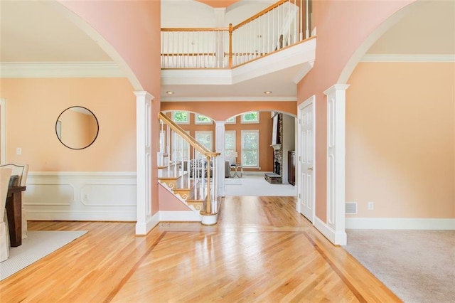 entryway with decorative columns, wood finished floors, a towering ceiling, and ornamental molding