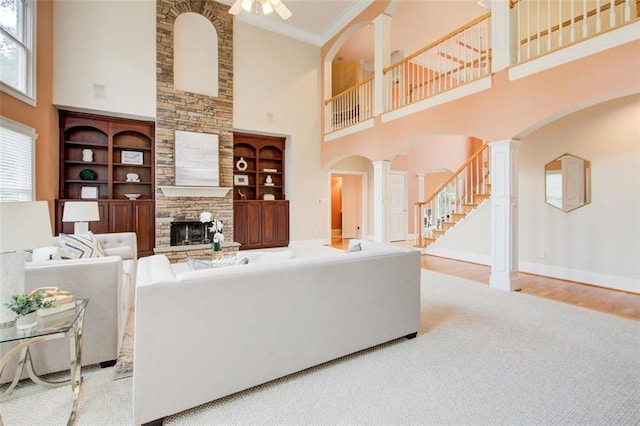 living area featuring stairway, wood finished floors, decorative columns, arched walkways, and a stone fireplace