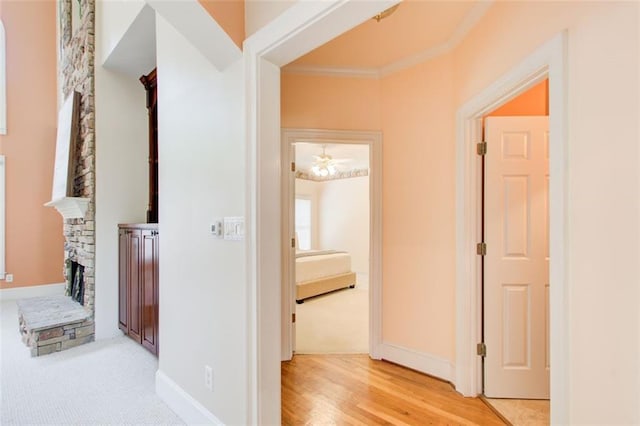 hall with light carpet, light wood finished floors, crown molding, and baseboards