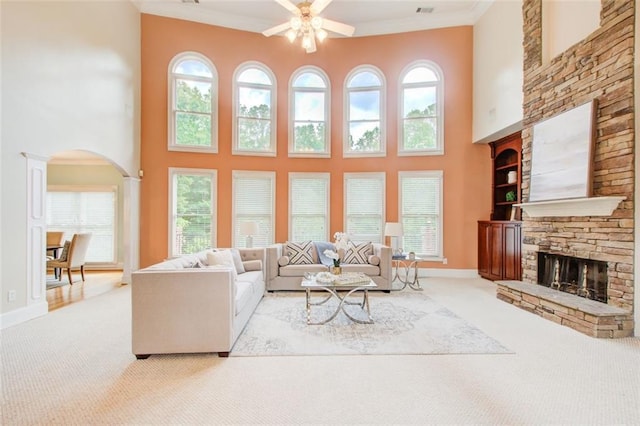 living room with crown molding, baseboards, carpet flooring, a stone fireplace, and arched walkways