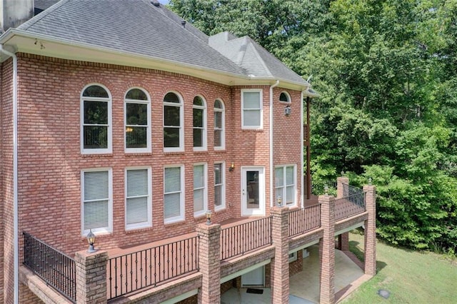 view of side of property featuring brick siding, a patio, and roof with shingles