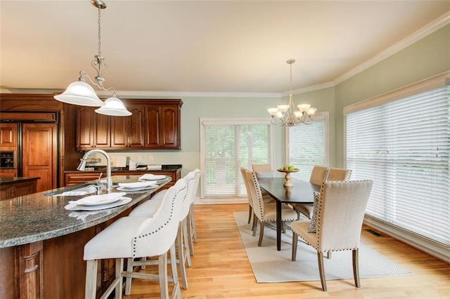 dining area featuring crown molding, visible vents, light wood-type flooring, and a chandelier