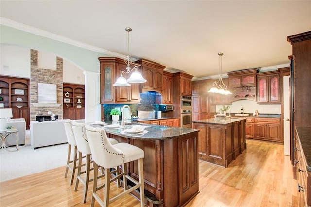 kitchen with crown molding, brown cabinets, a fireplace, a peninsula, and light wood-style floors