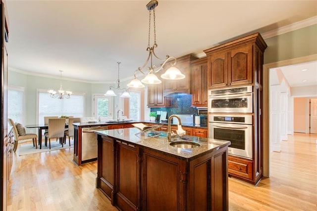 kitchen with an island with sink, light wood-style flooring, dark stone countertops, appliances with stainless steel finishes, and a sink