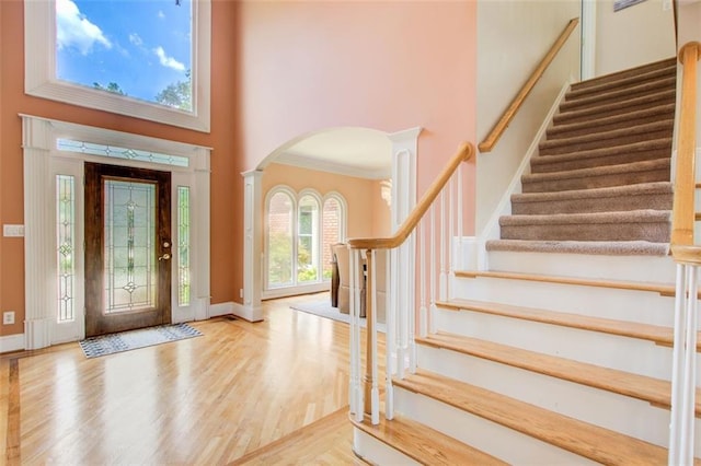 foyer entrance featuring wood finished floors, arched walkways, a towering ceiling, stairs, and ornate columns