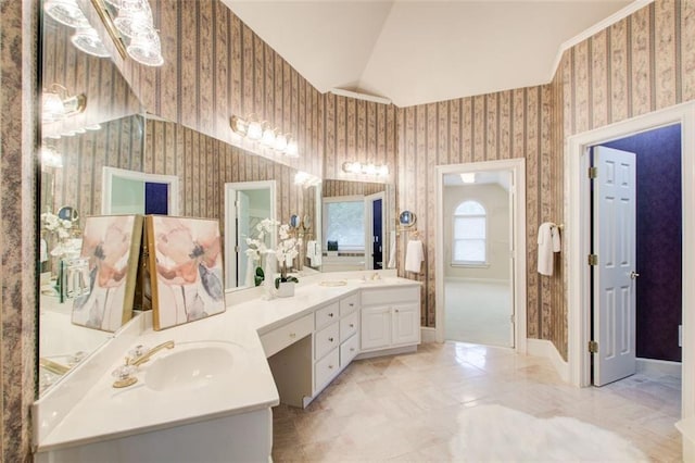 full bathroom featuring double vanity, a sink, wallpapered walls, and vaulted ceiling