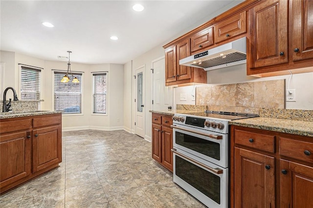 kitchen featuring sink, double oven range, backsplash, light stone counters, and decorative light fixtures