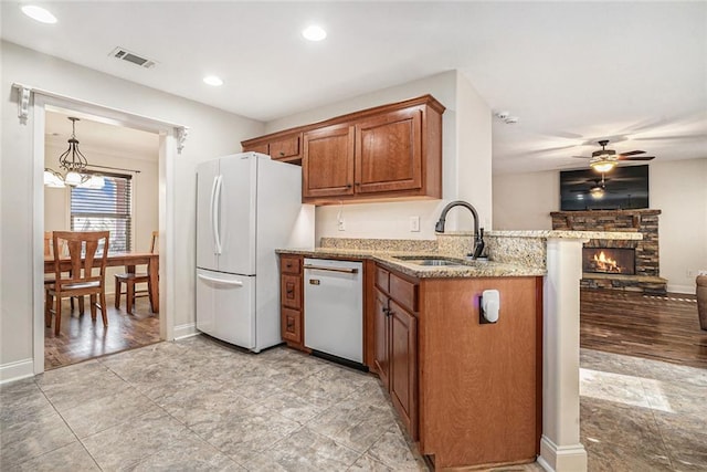 kitchen with sink, dishwasher, white refrigerator, a fireplace, and kitchen peninsula