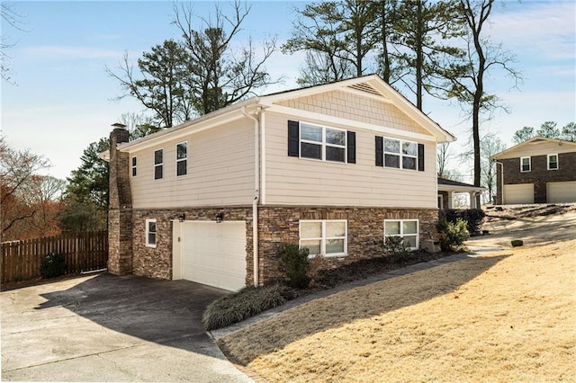 view of side of home with stone siding, fence, a garage, and driveway