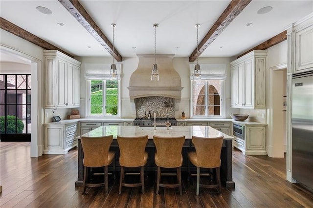 kitchen featuring built in appliances, light countertops, dark wood-style floors, custom exhaust hood, and a kitchen island with sink