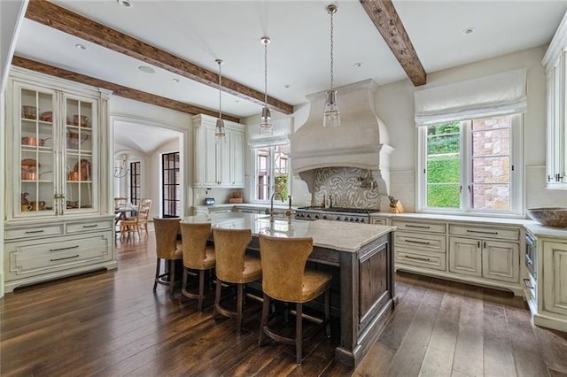 kitchen with beam ceiling, custom exhaust hood, an island with sink, and dark wood-style flooring