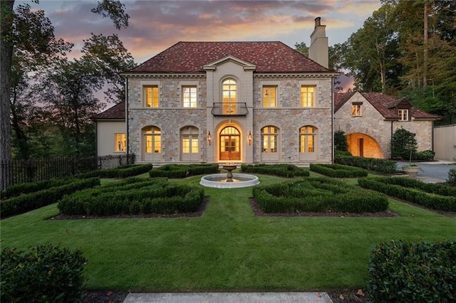 mediterranean / spanish house with a lawn, fence, french doors, a balcony, and a chimney