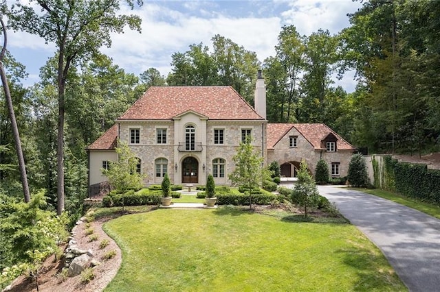 view of front of house featuring fence, a front yard, a chimney, stone siding, and driveway