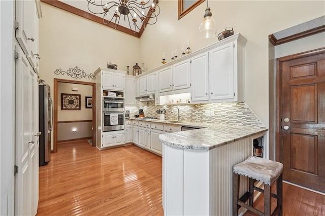 2011 Sturbridge Ln, Buford, GA 30519 - kitchen featuring a peninsula, stainless steel appliances, a chandelier, light wood finished floors, and high vaulted ceiling