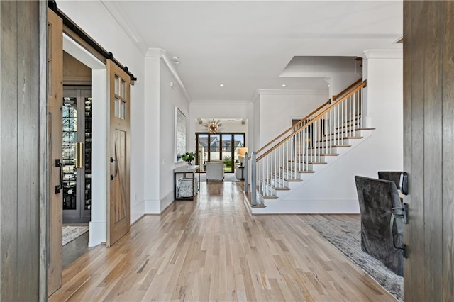 entrance foyer featuring light wood-type flooring, a barn door, and crown molding