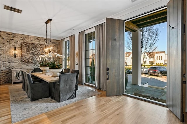 dining area featuring light hardwood / wood-style floors, crown molding, brick wall, and an inviting chandelier