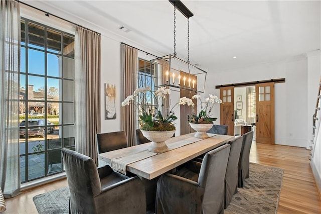 dining area featuring a barn door, light hardwood / wood-style floors, and an inviting chandelier