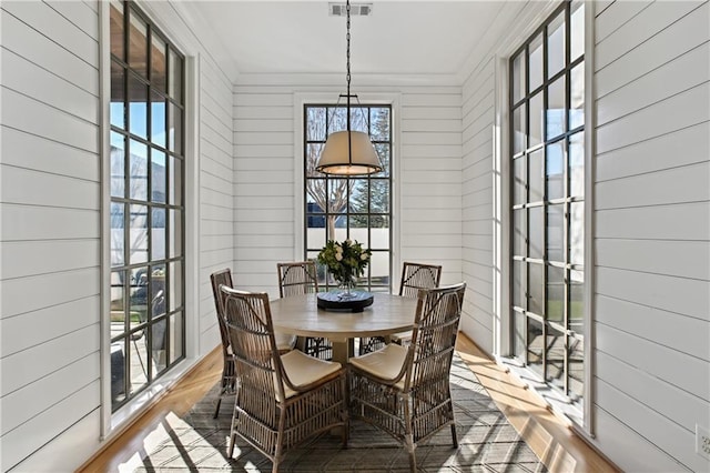 dining space with wood-type flooring, crown molding, and wooden walls