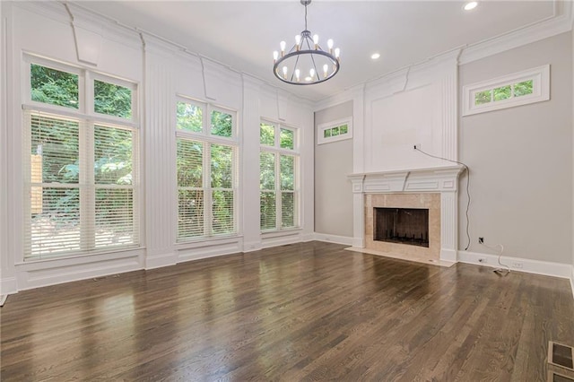 unfurnished living room with a tiled fireplace, ornamental molding, dark hardwood / wood-style floors, and an inviting chandelier