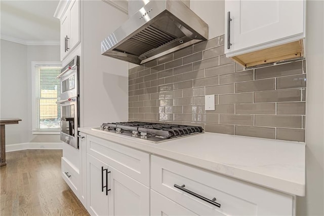 kitchen featuring white cabinetry, light hardwood / wood-style flooring, ornamental molding, stainless steel gas stovetop, and wall chimney range hood