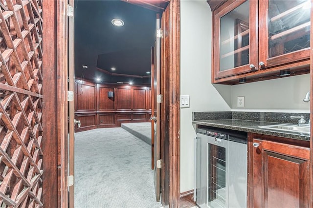 kitchen with wine cooler, sink, light colored carpet, and dark stone countertops