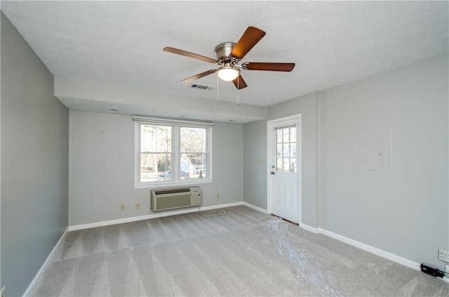 spare room with an AC wall unit, light colored carpet, ceiling fan, and a textured ceiling