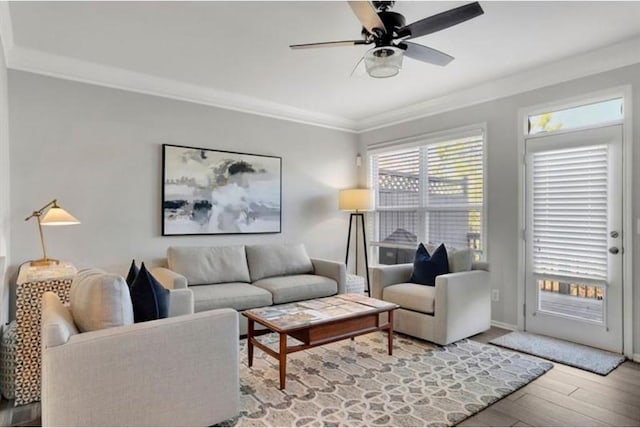 living area featuring crown molding, wood finished floors, baseboards, and ceiling fan