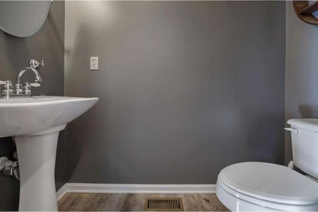 half bath with visible vents, baseboards, toilet, and wood finished floors