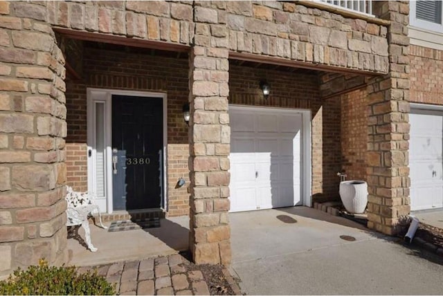 view of exterior entry featuring a garage, brick siding, and concrete driveway