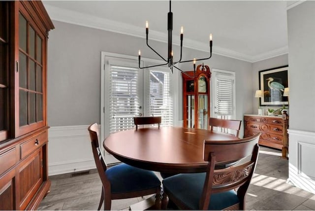 dining room with visible vents, light wood-style floors, wainscoting, crown molding, and a chandelier