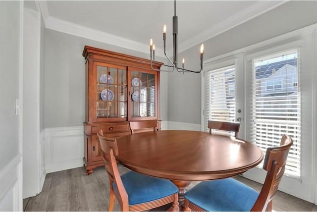 dining space with a wealth of natural light, an inviting chandelier, wainscoting, and crown molding