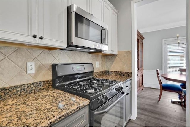 kitchen with stainless steel microwave, crown molding, dark stone countertops, wood finished floors, and black range with gas cooktop