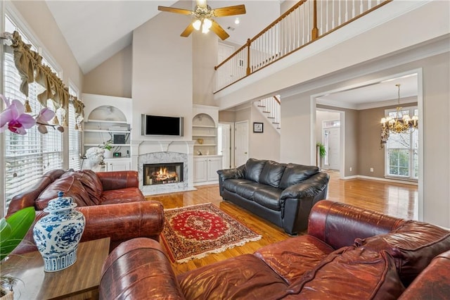 living area with built in shelves, wood finished floors, stairs, and ceiling fan with notable chandelier