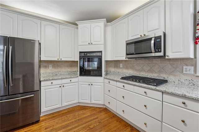 kitchen with light stone counters, tasteful backsplash, white cabinetry, appliances with stainless steel finishes, and light wood finished floors