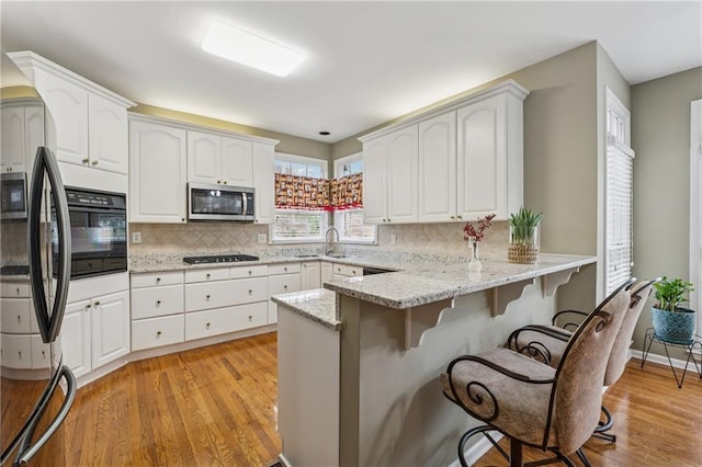 kitchen featuring stainless steel microwave, a kitchen breakfast bar, black oven, refrigerator, and a peninsula