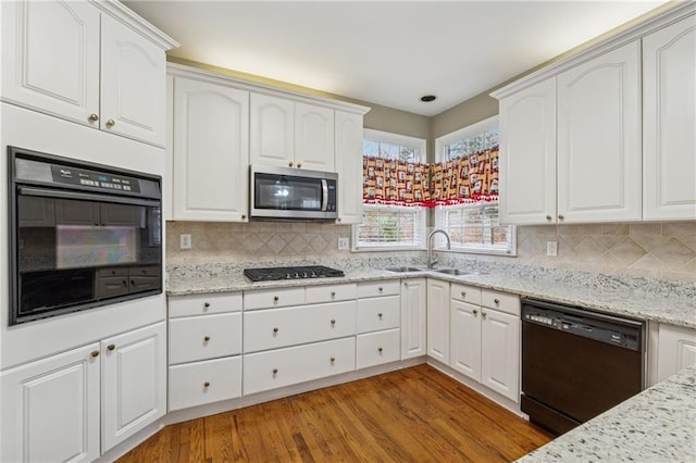 kitchen with black appliances, tasteful backsplash, light wood finished floors, and a sink