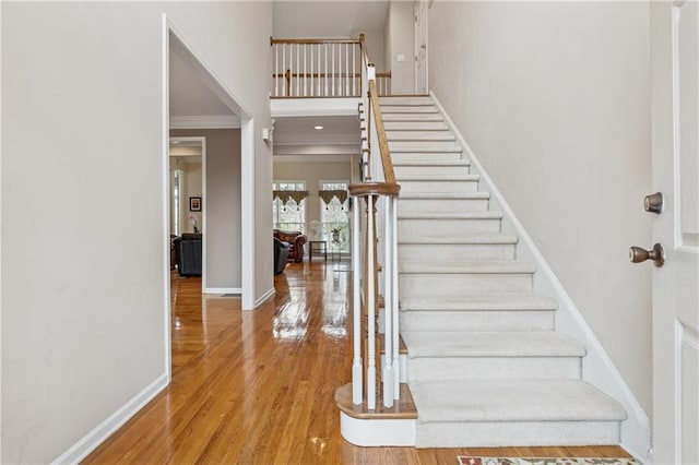 staircase featuring crown molding, wood finished floors, baseboards, and a towering ceiling