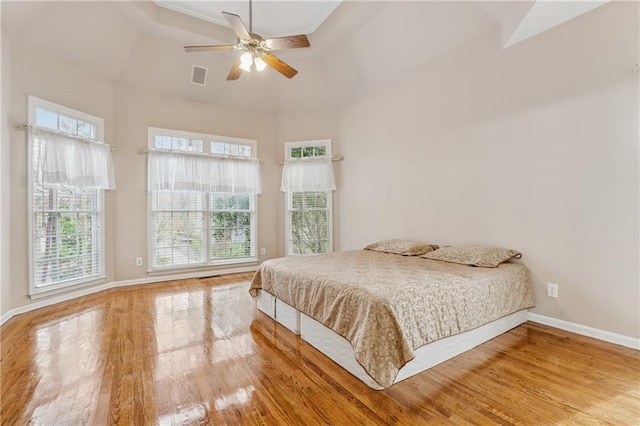 bedroom with visible vents, ceiling fan, baseboards, wood finished floors, and a raised ceiling